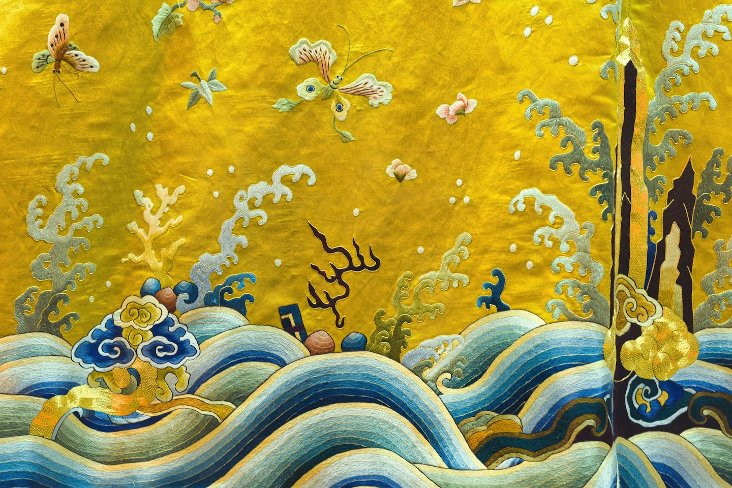 Intricate silk embroidery featuring waves, clouds, butterflies, and flowers on fabric.