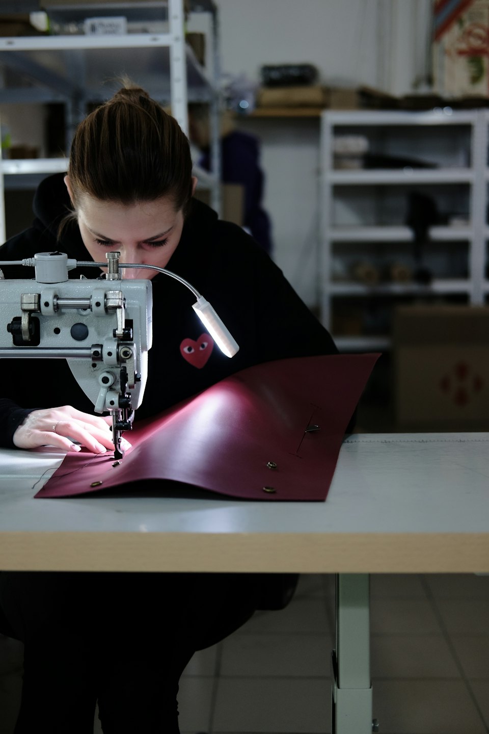 Woman sewing red leather on a sewing machine.